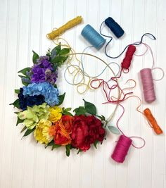 several spools of thread and colorful flowers on a white tablecloth with yarn