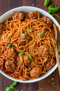 spaghetti with meatballs and tomato sauce in a white bowl on a wooden table top