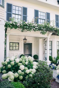 a white house with blue shutters and flowers in front