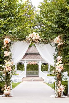 an outdoor wedding ceremony with white chairs and pink flowers on the arch over the aisle