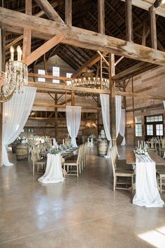 the inside of a barn with tables, chairs and chandeliers