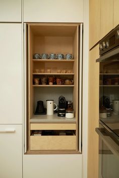 an open cabinet in a kitchen with coffee pots and mugs