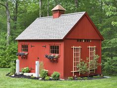 a red shed with two windows and plants on the roof is in front of trees