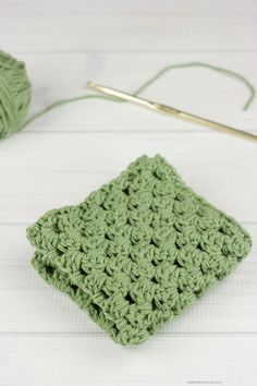 a green crochet square sitting on top of a white table next to a pair of knitting needles