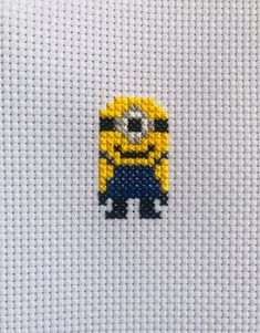 a cross stitch minion with yellow and blue beads on it's face, sitting in front of a white background