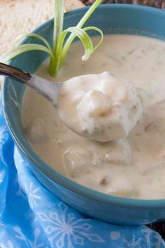 a spoon full of clam chowder in a blue bowl on a blue cloth