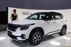 a woman standing next to a white suv on display at an auto show in front of a wall