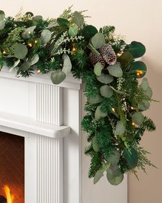 a mantel decorated with greenery, pine cones and evergreen leaves is lit by the fireplace