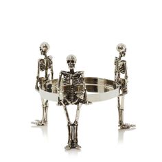 three skeleton figurines sitting on top of a silver tray with one holding the other