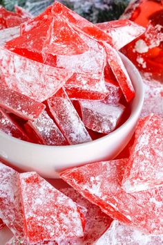 a white bowl filled with red sugar cubes on top of snow covered ground next to christmas decorations