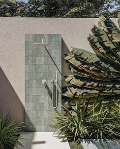 an outdoor shower in the middle of a garden with trees and plants around it, next to a concrete wall