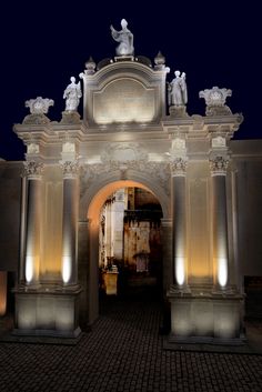 an arch with statues on it lit up at night