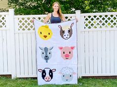 a woman standing next to a fence holding up a quilt with farm animals on it