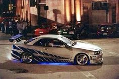 a silver car with blue stripes on it parked in front of a building at night