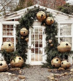 a white shed with christmas decorations on the front and side windows, surrounded by rocks