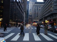 people crossing the street in front of tall buildings