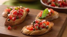 three pieces of bread with tomatoes and capers on them sitting on a cutting board