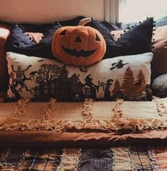 a pumpkin pillow sitting on top of a bed next to pillows with halloween decorations around it