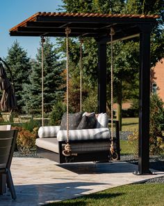 an outdoor swing bed with cushions on it in the middle of a patio area next to a table and chairs