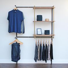 a clothes rack with clothing hanging on it next to a wall mounted coat hanger