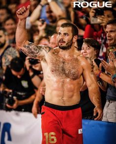 a man with no shirt on standing in front of a crowd holding his arm up