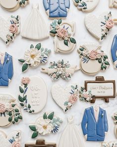 wedding cookies are arranged on a white tablecloth with flowers and groom's suits