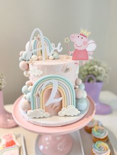 a pink and blue cake with pep the pig on top is surrounded by cupcakes