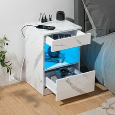 a nightstand with two drawers and an electronic device on it next to a plant in a bedroom