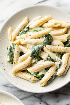 a white bowl filled with pasta and spinach on top of a marble countertop