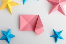 three origami stars on a white surface with one folded in pink, one blue and one yellow