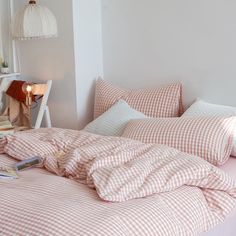 an unmade bed with red and white checkered comforter on it, next to a night stand