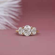 three stone diamond ring on pink background with feathers in the backgroufground