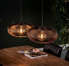 three lights hanging from the ceiling above a wooden table with leather chairs and a magazine on it