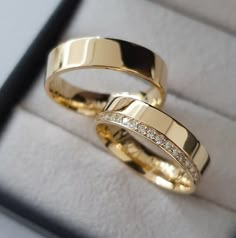 two gold wedding rings sitting in a white box with diamonds on it's sides