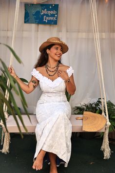 a woman in a white dress and hat sitting on a swing