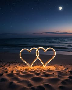 two heart shaped lights sitting in the sand on a beach at night with moon and stars