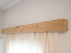 a wooden shelf above a window in a room with white walls and drapes on the windowsill