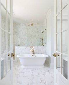 a white bathroom with marble floors and walls, along with a freestanding bathtub