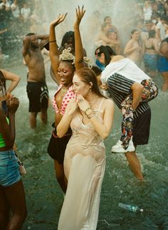 two women are dancing in the water at a music festival with other people behind them