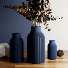 three blue vases sitting on top of a wooden table next to each other with flowers in them