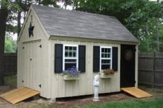 a small white shed with black shutters on the windows, and a flower box in front