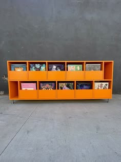 an orange shelf with books on it sitting in front of a gray wall and concrete floor