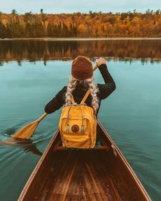 a woman in a yellow backpack paddling a canoe on the water with her back to the camera