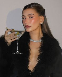 a woman holding a martini glass in her hand and wearing a black fur coat over it