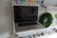 a laptop computer sitting on top of a white shelf next to a wreath and magnets