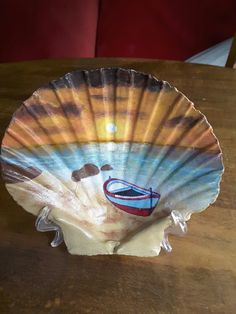 a paper plate shaped like a shell with a boat painted on the inside and bottom