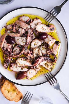 an octopus dish on a plate with olives, bread and silverware next to it