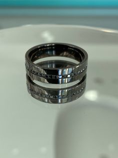 two wedding bands sitting on top of a white table with blue glass in the background