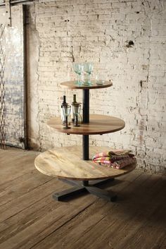 three tiered table with bottles on it in front of a brick wall and wooden floor