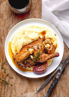 a white plate topped with meat and mashed potatoes next to a glass of wine